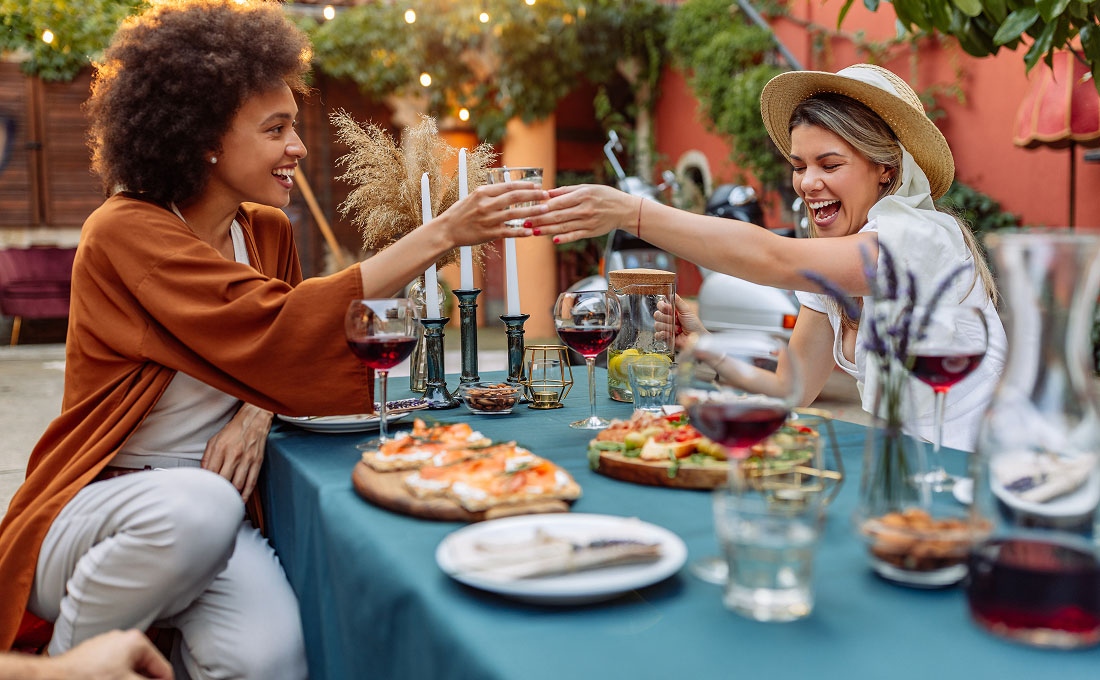 Two women toast while eating a meal outdoors